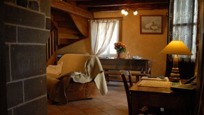 Une pièce chaleureuse avec une cheminée, une table à manger avec des chaises, une fenêtre avec des rideaux et une lampe.