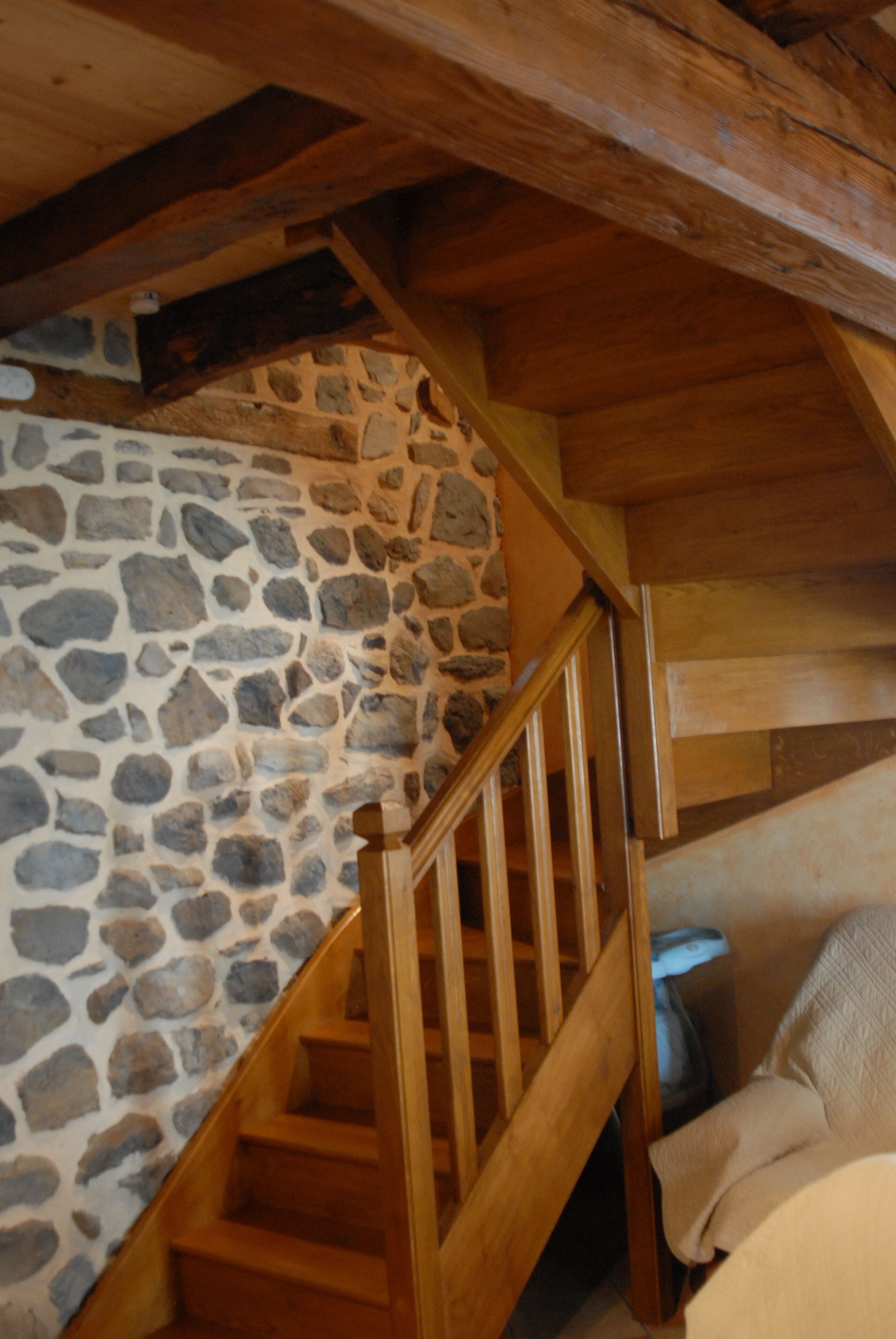 A wooden staircase with a stone wall on one side and a bed with a white cover at the bottom.
