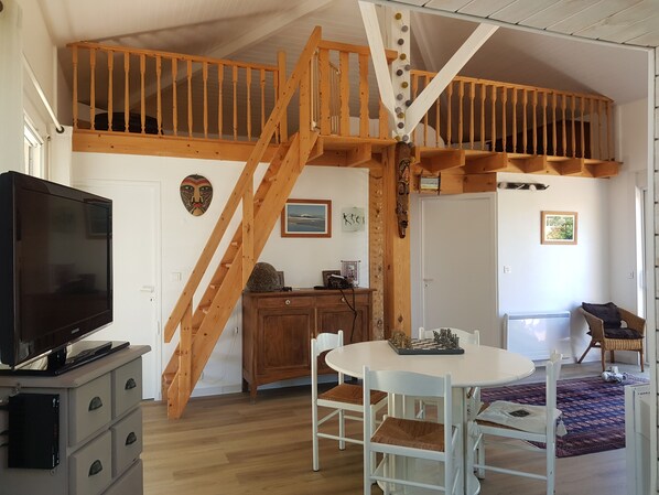Amplia sala de estar con una escalera de madera, televisor, mesa de comedor con sillas y un rincón de estar acogedor.