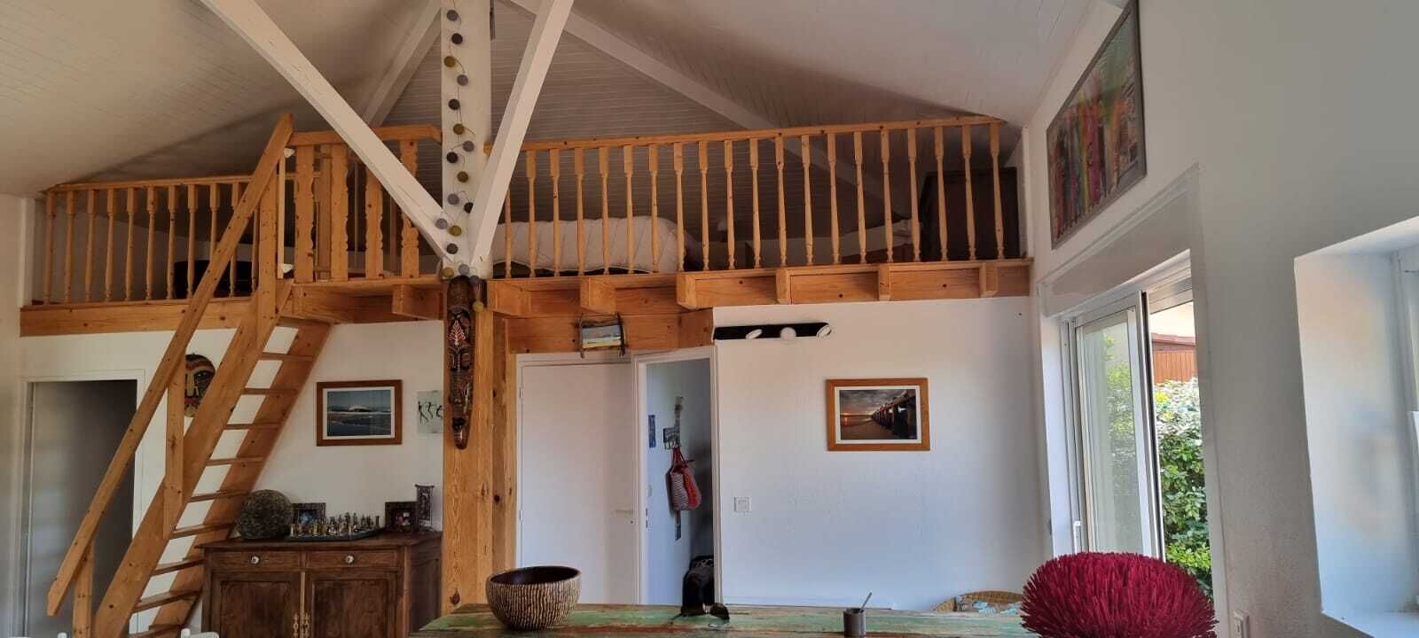 Quarto no estilo loft com escada de madeira, cama no mezanino e vista para o exterior.