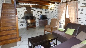 Sala de estar com parede de pedra, escada de madeira, lareira, televisão, sofá e mesa de centro.