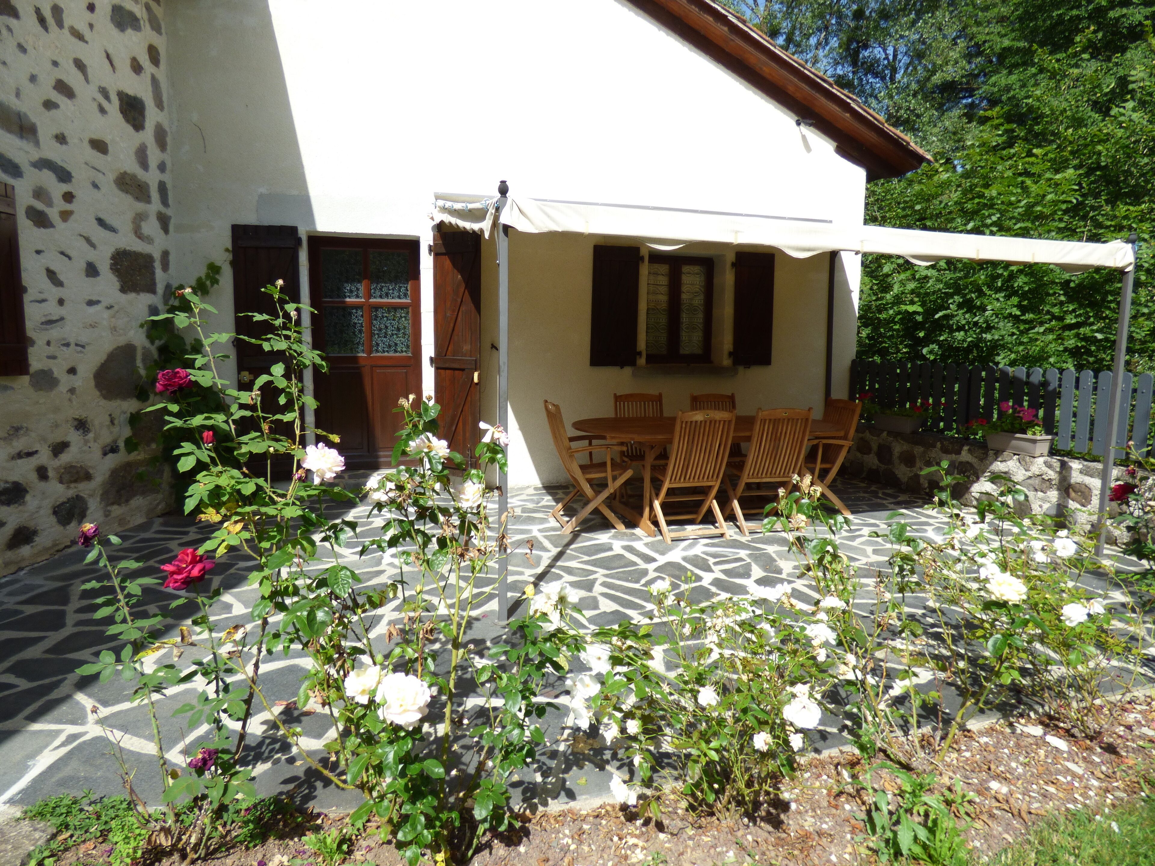 Edificio de piedra con un patio empedrado, muebles de madera y plantas con flores.
