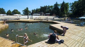 Piscina com decks de madeira, rodeada por árvores e uma área de praia arenosa.
