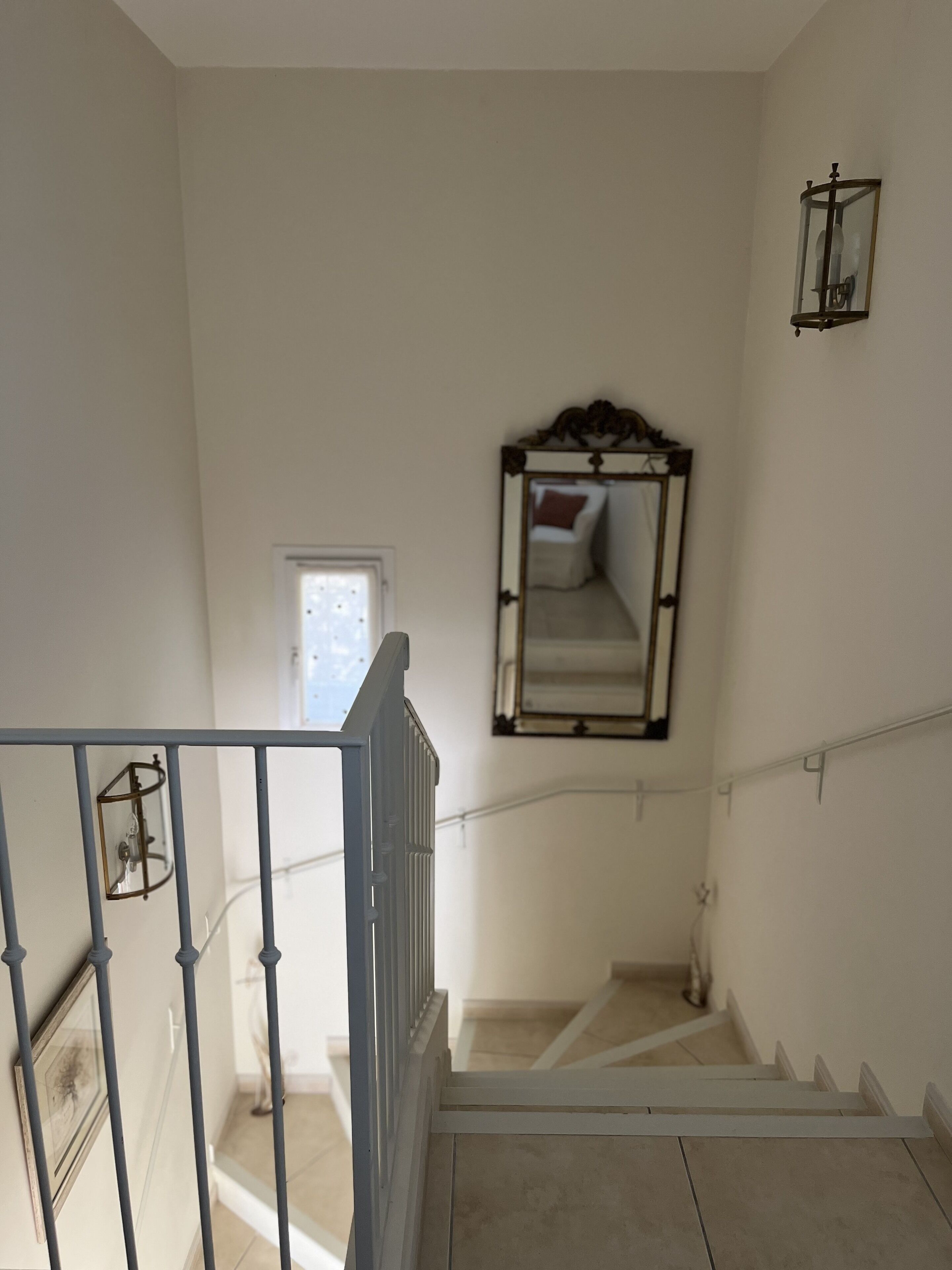 Una escala amb barana, mirall i un llum penjada a la paret.