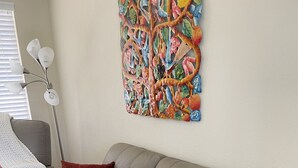 Un salon moderne avec un canapé en cuir gris, de nombreux coussins, une lampe sur pied et une peinture abstraite aux couleurs vives accrochée au mur.