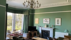 Ein Wohnzimmer mit grünen Wänden, einem Kamin, einer Chandelüster und einem Essbereich mit Blick auf Bäume.