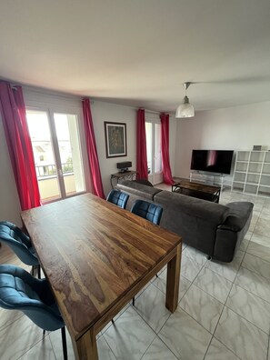 A modern living room with a wooden dining table, blue chairs, a grey sofa, and a TV. - SOLENZARA CENTER Apartment (Sari-Solenzara)