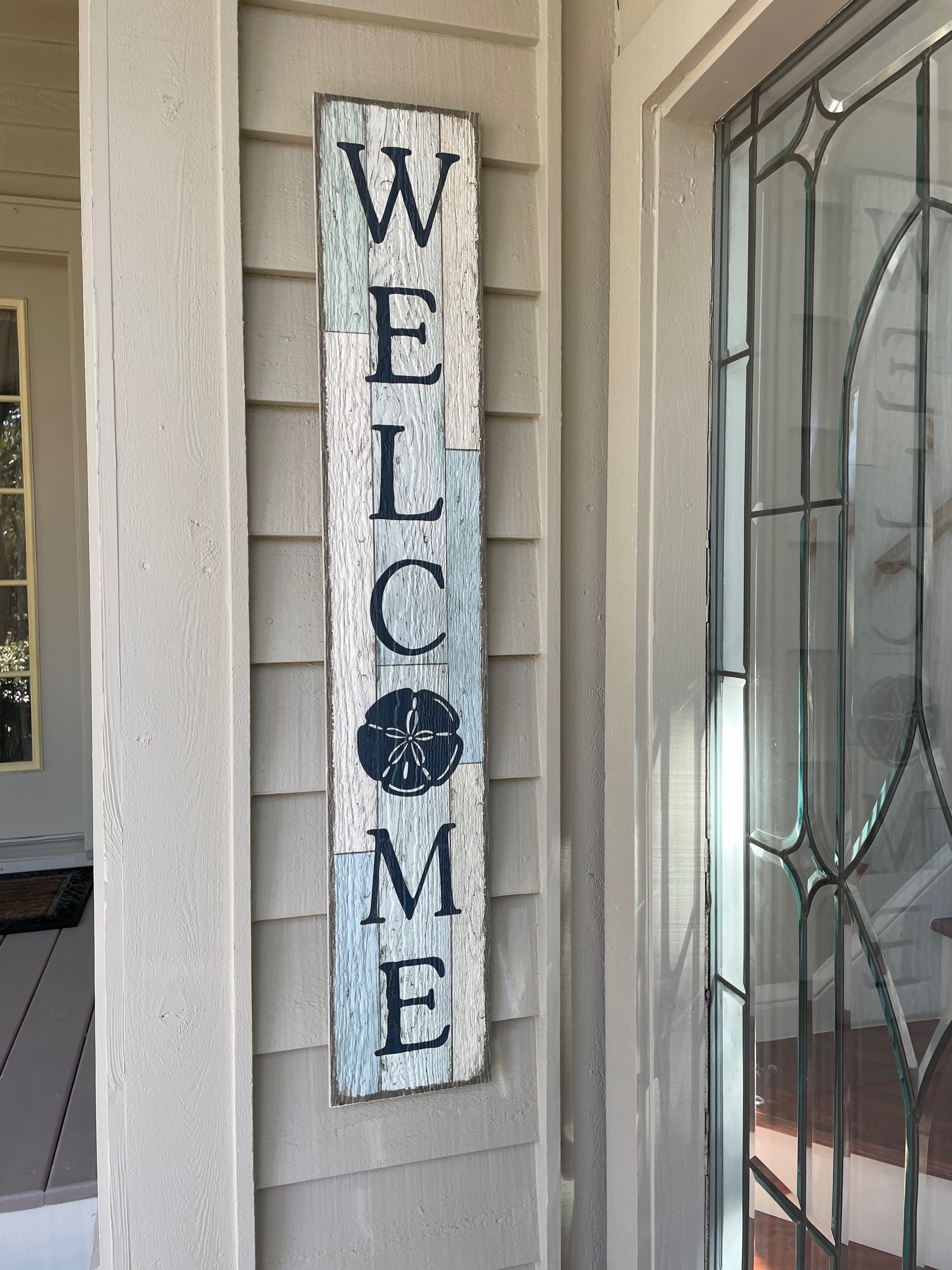 A wooden welcome sign with the letters "WELCOME" and a decorative emblem on a house's exterior wall.