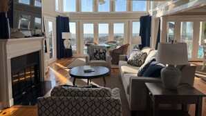 Un salon spacieux doté d’une cheminée, de sièges confortables et de grandes fenêtres offrant une vue sur l’extérieur.