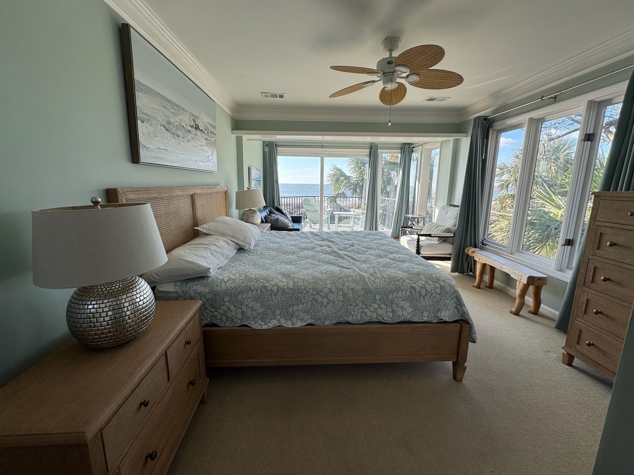 A bedroom with a bed, a dresser, a lamp, a ceiling fan, and a view of the outdoors.