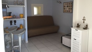 A compact living space with a brown sofa, a white cabinet, and a small dining area with stools and a fan. - LOCATION DUPLEX 4 PERS. 45M2 NEAR SAINTE MAXIME VAR ..IDEALEMENT LOCATED ... (Le Muy)
