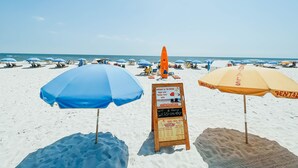 Une plage avec des parasols et un panneau indiquant les locations de matériel de plage.