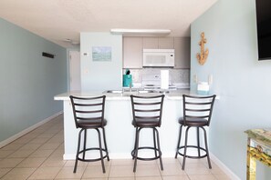 A kitchen with a white island, three bar stools, a microwave, and a sink. - Gulf View Sugar Beach Condo - 1BR with Loft - Beachfront Pools - Sleeps 4 (Orange Beach)