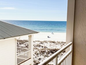 A beach view from a balcony with a railing, a beach umbrella, and a lifeguard stand. - Gulf View Sugar Beach Condo - 1BR with Loft - Beachfront Pools - Sleeps 4 (Orange Beach)