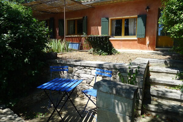 A house with a stone wall, a wooden deck, and a blue folding chair. - Charming Mazet, completely renovated, very quiet, in pine forest, near the center (Nîmes)