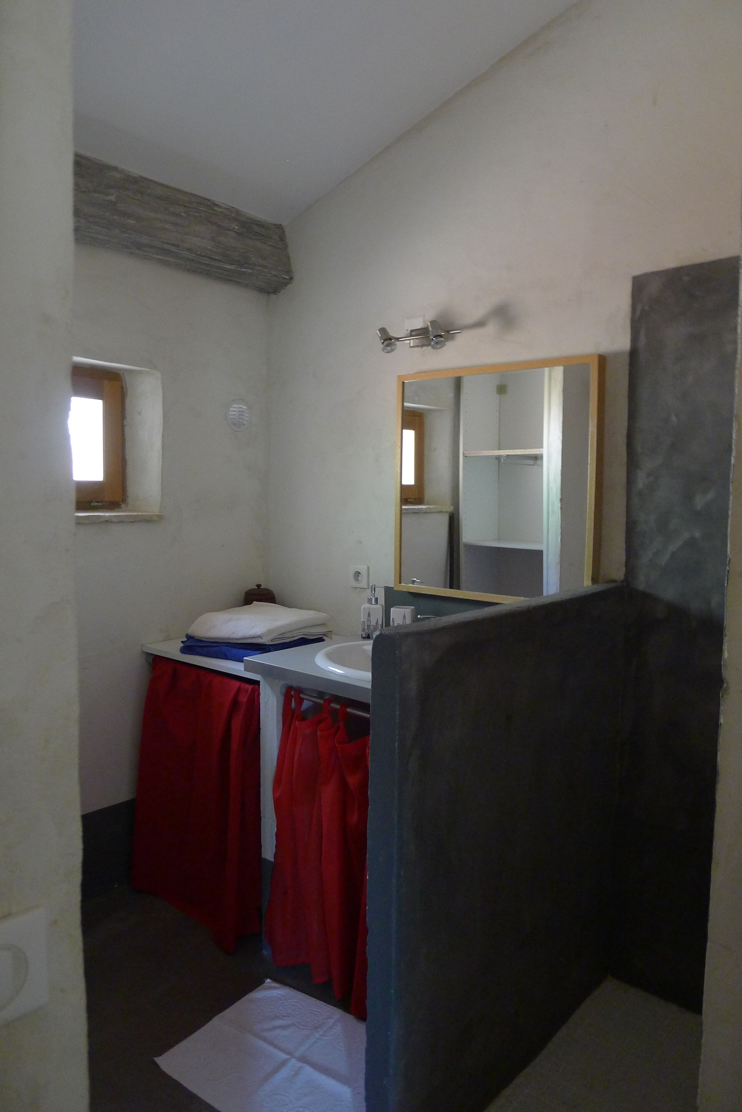 Une petite salle de bain avec un lavabo blanc, un miroir et des serviettes rouges.