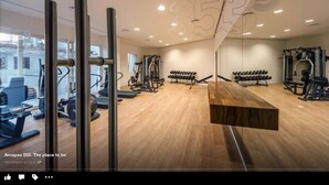 Un gimnasio moderno con piso de madera, diversos equipos de ejercicio y un espejo grande.
