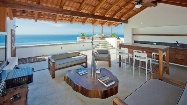 Amplio espacio exterior con techo de madera, mesa de comedor y zona de estar con vistas al océano.