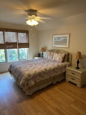 A bedroom with a bed, two nightstands, a ceiling fan, a window with blinds, and a framed picture on the wall.