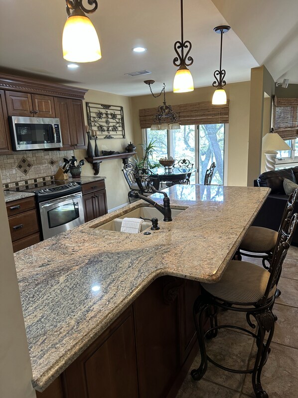 A kitchen with granite countertops, stainless steel appliances, and dark wooden cabinets. There is a dining area with a table and chairs, and a view of trees outside. - Turtle Cove Open Floor Plan 2bed/2bath Turtle Cove Villa Pet Friendly (Kiawah Island)