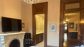 A bedroom with a large bed, a fireplace, a TV, and a view into the bathroom. - Close to NYC in Historic Brownstone (Jersey City)