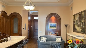 A dining area with a wooden table and chairs, a blue sofa with patterned cushions, and a vase with flowers on a table. - Close to NYC in Historic Brownstone (Jersey City)