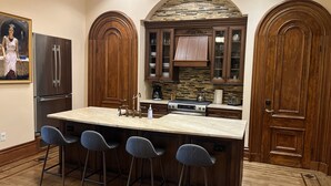 A kitchen with a large island, bar stools, wooden cabinets, a stone backsplash, and a refrigerator. - Close to NYC in Historic Brownstone (Jersey City)