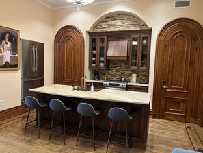 Una cucina con una grande isola, sgabelli da bar, mobili in legno, una schiena di pietra e un frigorifero.