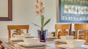 Een eettafel gedekt met witte borden, kommen en een paarse vaas met bloemen.