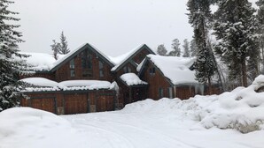 Una casa de madera grande con un tejado empinado, rodeada de árboles cubiertos de nieve.