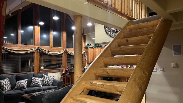 Una escalera en espiral de madera en un interior moderno, con un sofá de color oscuro y una zona de comedor al fondo.