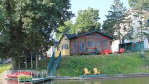 Una cabaña junto al lago con muelle, mobiliario exterior y un bote pequeño.