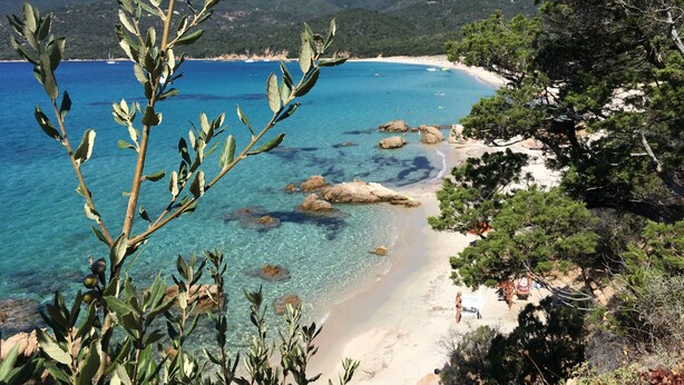 A coastal landscape with clear waters, a sandy beach, and rocky outcrops.