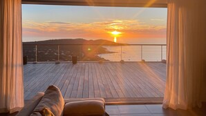 A balcony with a wooden floor, a sofa, and a view of the sunset over the sea.