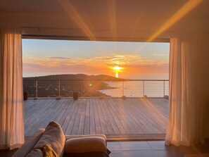 Un balcón con piso de madera, un sofá y vistas al atardecer sobre el mar.