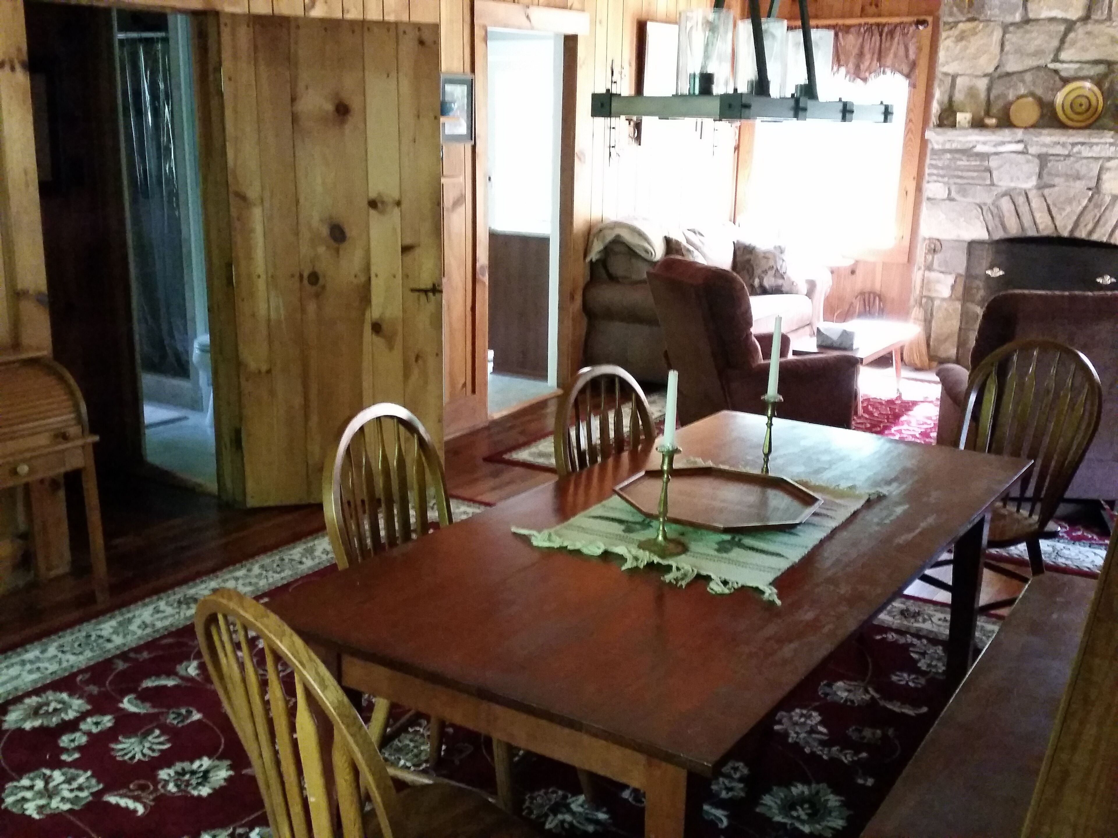 A wooden dining room with a table and chairs, a fireplace, and a stone wall.