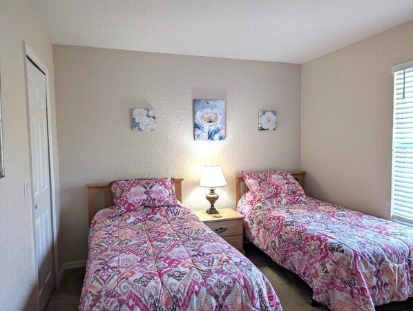 A bedroom with two beds, a nightstand with a lamp, and three wall-mounted paintings.