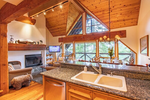 A kitchen with granite countertops, a double sink, wooden cabinets, a fireplace, and large windows offering a view of the outdoors. - Pinnacle Ridge 37 - Ski in Ski out, Private Hot Tub, Wood Fireplace (Whistler)