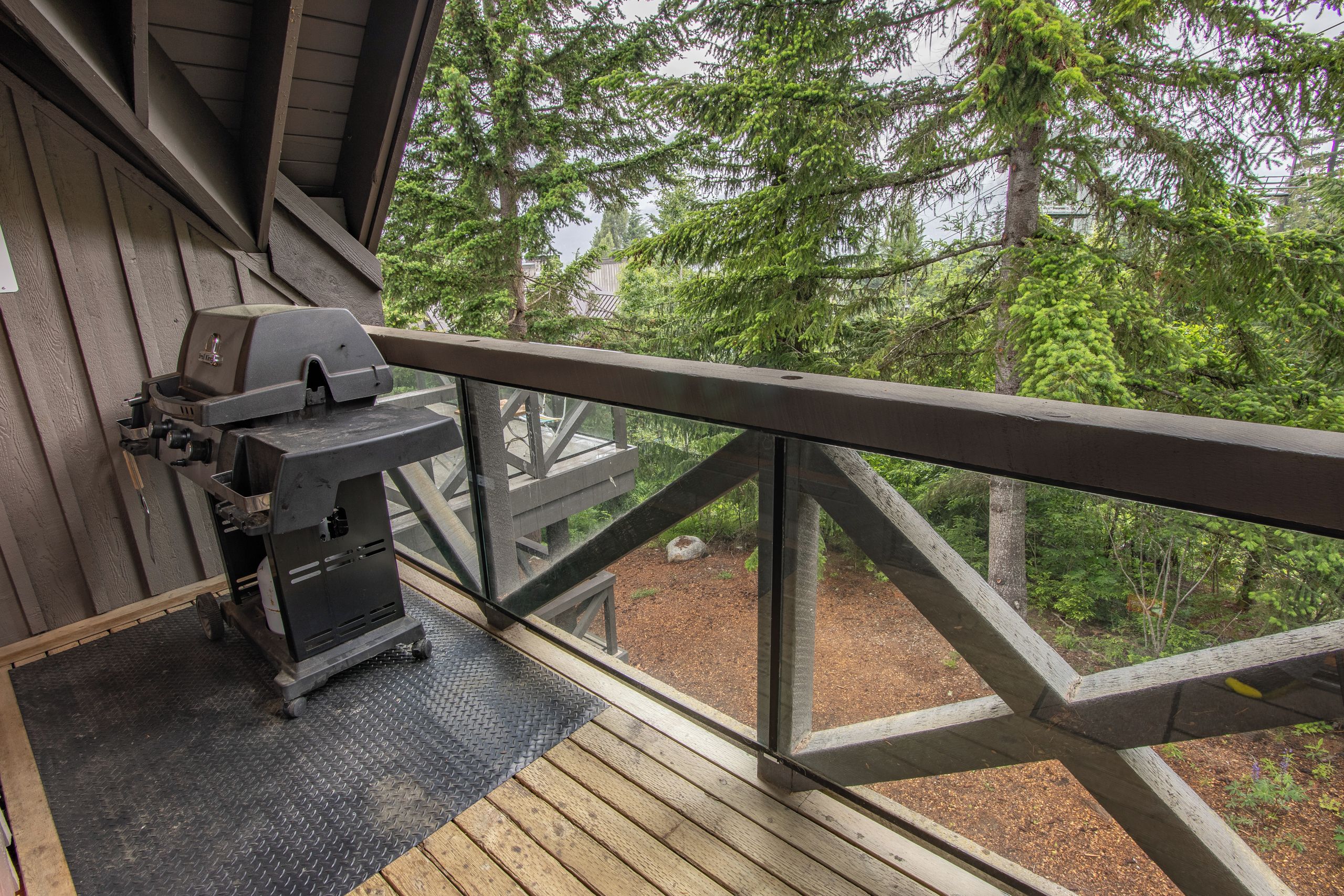 Eine Holzterrasse mit Grill und Blick auf einen Wald.