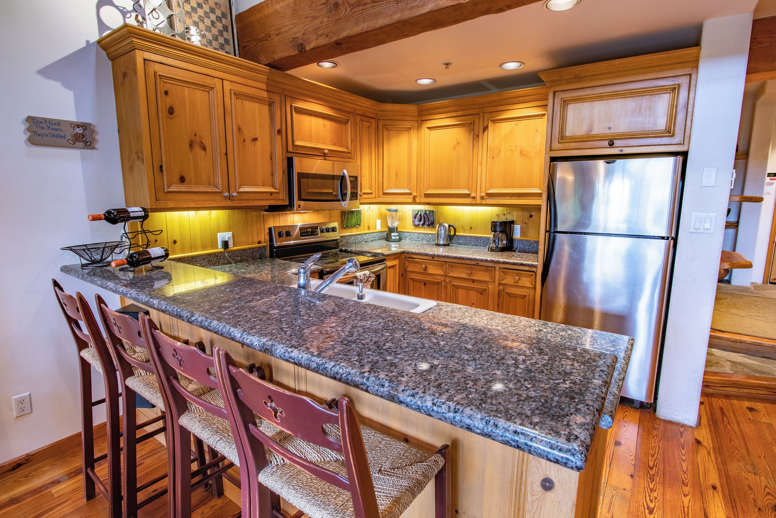 A kitchen with wooden cabinets, granite countertops, stainless steel appliances, and bar stools.