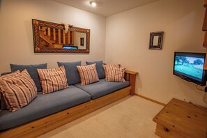 A cozy living room with a blue sofa, striped pillows, a wooden coffee table, a television, and a decorative mirror. - Pinnacle Ridge 37 – Ski in Ski out, Private Hot Tub, Wood Fireplace (Whistler)