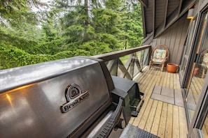 A grill on a wooden deck with a view of dense forest. - Pinnacle Ridge, 3 Bedroom + Den (Whistler)