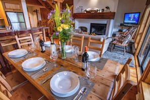 A wooden dining table set with plates, cutlery, and a vase of flowers. - Pinnacle Ridge 37 – Ski in Ski out, Private Hot Tub, Wood Fireplace (Whistler)