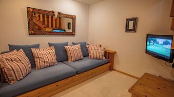 A cozy living room with a blue sofa, striped pillows, a wooden coffee table, a television, and a decorative mirror.