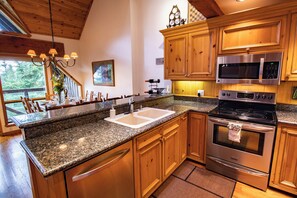 A kitchen with granite countertops, wooden cabinets, stainless steel appliances, and a large window overlooking a deck. - Pinnacle Ridge 37 – Ski in Ski out, Private Hot Tub, Wood Fireplace (Whistler)
