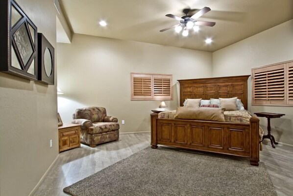 A bedroom with a large bed, a wooden headboard, a ceiling fan, and a carpeted floor. - Large Balcony, Exceptional Views. (Tucson)