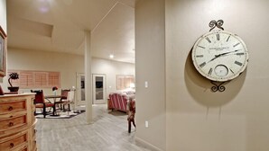 A spacious living area with a large wall clock, a wooden dresser, and a dining area with chairs and a table. - Large Balcony, Exceptional Views. (Tucson)