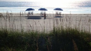 A beach with three umbrellas and lounge chairs.