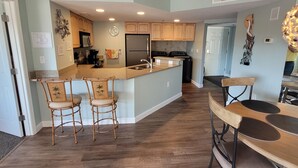 A modern kitchen with wooden cabinets, a central island with bar stools, and a dining area with a table and chairs.