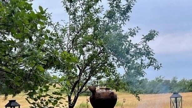 Un entorno rústico al aire libre con una estructura de piedra, una olla de barro grande y dos faroles.
